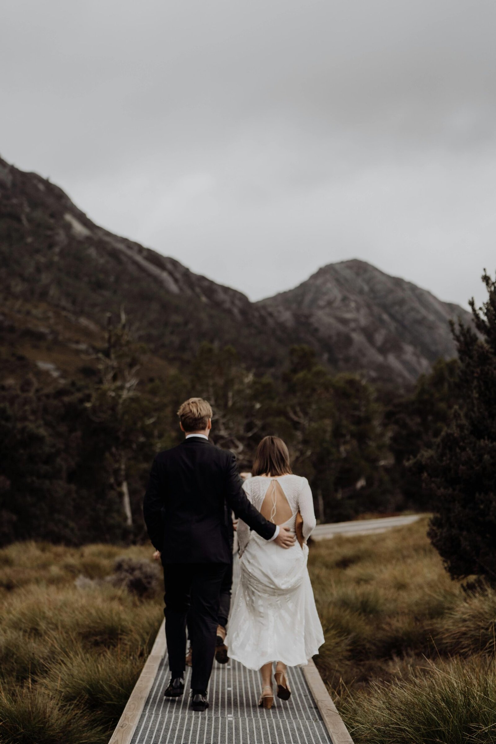 Newlywed couple walking through Cradle Mountain scenery in overcast weather.