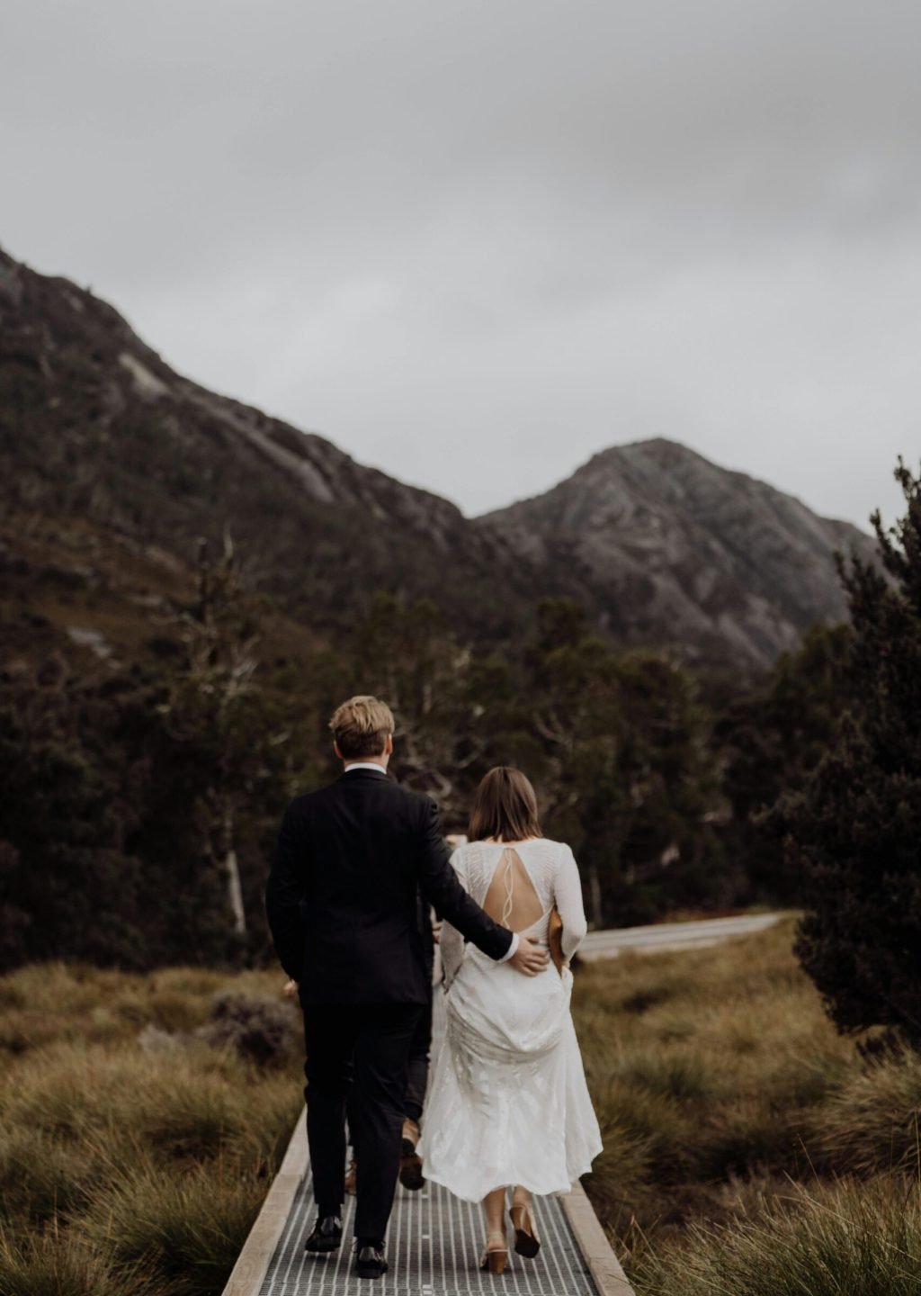 Newlywed couple walking through Cradle Mountain scenery in overcast weather.